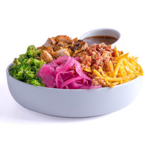 White bowl with grilled chicken, broccoli, pickled red onions, bacon bits, shredded cheddar cheese, and a small cup of brown dressing on a light gray background.