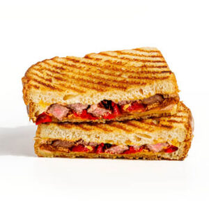 Grilled panini sandwich cut in half and stacked, filled with sliced steak, red peppers, and melted cheese on a light gray background.