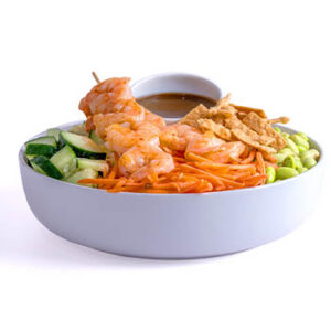 White bowl with shrimp, cucumber, shredded carrots, edamame, crispy wonton strips, and a small cup of brown sauce on a light gray background.